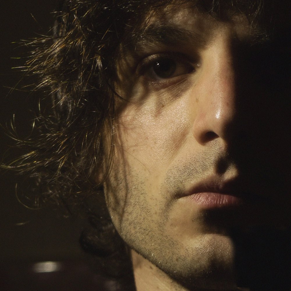 Portrait of John-Paul James, lit from one side against a dark background.